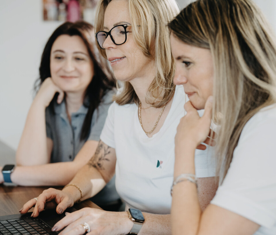 Marina Hartmann, Andrea Hirschberger und Tanja Breyer sitzen gemeinsam an einem Tisch und schauen auf ein Laptop.