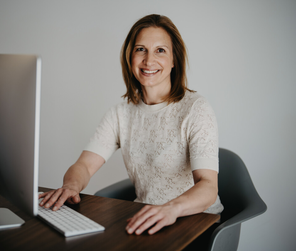 Christiane Berger sitzt vor einem Desktop und l&auml;chelt in die Kamera.