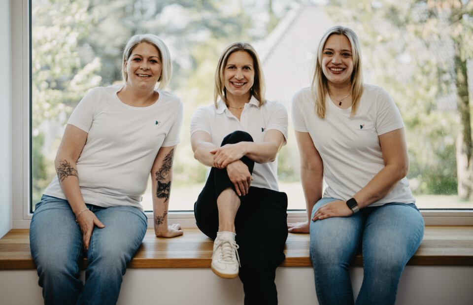 Von links nach rechts: Charlene Antes, Christina Berger und Jana Hellmann sitzen entspannt nebeneinander auf einer h&ouml;lzernen Fensterbank.