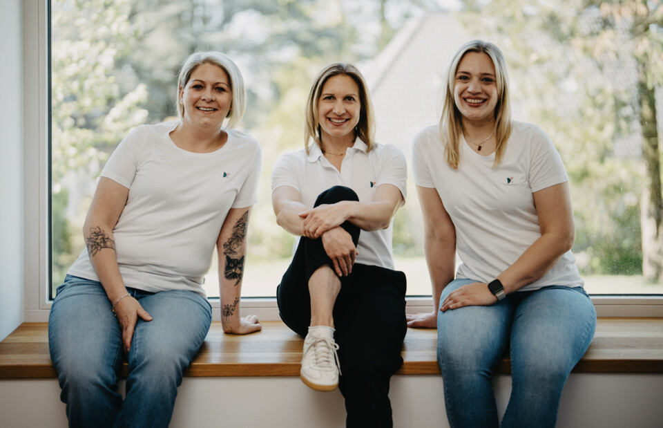 Von links nach rechts: Charlene Antes, Christina Berger und Jana Hellmann sitzen entspannt nebeneinander auf einer h&ouml;lzernen Fensterbank.